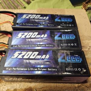 A stack of three high capacity Zeee 3S 11.1V 5200mAh 80C hardcase LiPo packs on an RC hobby workbench.